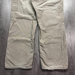 Puede incluir: Primer plano de un pantal&oacute;n de trabajo color caqui. El pantal&oacute;n tiene un dise&ntilde;o de pierna recta y un bolsillo utilitario en el lado derecho. La tela parece ser una mezcla de algod&oacute;n duradera, con desgaste visible en el dobladillo.