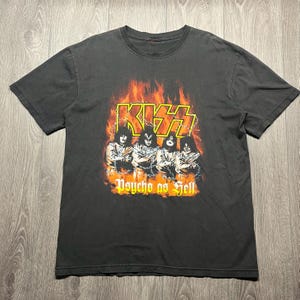 Peut inclure: T-shirt gris foncé avec le groupe KISS sur un fond enflammé. Le logo du groupe est jaune et le texte "Psycho as Hell" est en dessous des membres du groupe.