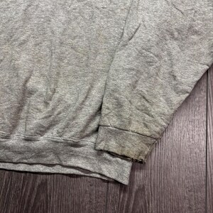 Puede incluir: Primer plano de una manga de sudadera gris. El pu&ntilde;o est&aacute; desgastado y descolorido. La tela es gris jaspeado, mostrando signos de desgaste y uso. La sudadera parece estar hecha de un material suave y c&oacute;modo.