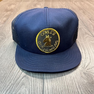 May include: A navy blue trucker hat with a black and gold patch that says "Coyles of Tillsonburg".