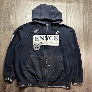 Peut inclure: Un sweat à capuche zippé bleu marine foncé avec un grand écusson rectangulaire crème sur la poitrine portant le texte ENYCE. Le vêtement comprend une capuche avec cordons de serrage, deux poches avant et des écussons circulaires brodés.