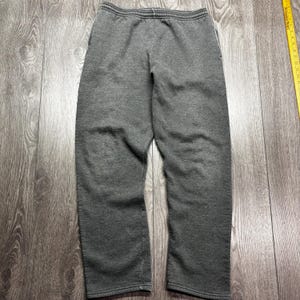 Könnte beinhalten: Anthrazitfarbene Jogginghose mit elastischem Bund und Kordelzug. Die Hose ist aus einem weichen, bequemen Material gefertigt, ideal für Freizeitkleidung. Die Jogginghose wird auf einer Holzoberfläche gezeigt.