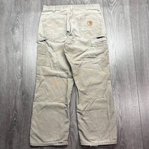 Puede incluir: Pantalones de trabajo color caqui con m&uacute;ltiples bolsillos, incluyendo dos bolsillos traseros y un bolsillo lateral. Los pantalones tienen un dise&ntilde;o de pierna recta y un peque&ntilde;o parche cuadrado con el logo en el bolsillo trasero. La tela parece duradera y ligeramente desgastada.