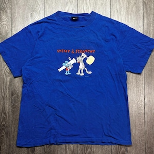 Könnte beinhalten: Blaues T-Shirt mit den Zeichentrickfiguren Itchy und Scratchy. Itchy, eine blaue Maus, hält ein weißes Objekt, während Scratchy, eine graue Katze, ein gelbes Objekt schwingt. Der Text "ITCHY & SCRATCHY" steht über den Figuren.