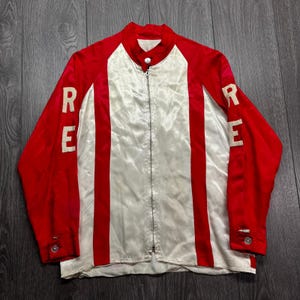 May include: A vintage red and white satin jacket with the word "RE" on each sleeve. The jacket has a zipper closure and a stand-up collar. The sleeves and side panels are red, while the front and back panels are white with red stripes.