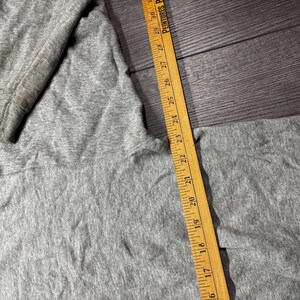 Puede incluir: Primer plano de una sudadera gris con una regla de madera que mide de 40,6 a 76,2 cm. La regla tiene el texto "PEINTURES P" impreso. La sudadera est&aacute; sobre una superficie de madera gris oscura.
