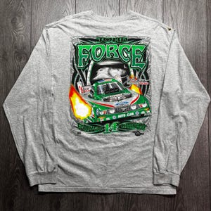 May include: A heather gray long-sleeve t-shirt featuring a graphic on the back of a green and white John Force Funny Car race car with flames. The text reads John Force, Funny Car 14 Champion, and includes a signature and racing logos.