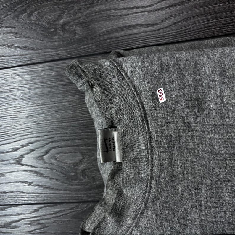 Puede incluir: Una camiseta gris de cuello redondo con una etiqueta que dice "Nike Sports Car Costa". Tambi&eacute;n es visible una peque&ntilde;a etiqueta blanca con el n&uacute;mero "5K63". La camiseta est&aacute; hecha de un material suave y c&oacute;modo.