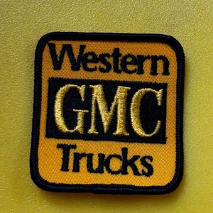 May include: Embroidered patch with the text "Western GMC Trucks." The patch is square with rounded corners. The background is yellow, with black and gold lettering. The border is black.