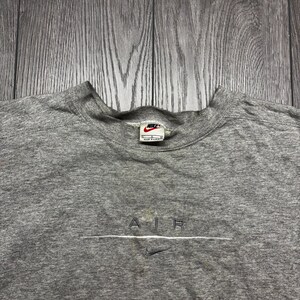 Puede incluir: Una sudadera gris jaspeado con cuello redondo y el logo de Nike en el cuello. La palabra "AIR" est&aacute; bordada en blanco en el pecho, con un peque&ntilde;o logo de Nike swoosh debajo. La sudadera est&aacute; hecha de un material suave y c&oacute;modo.