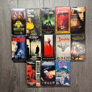 Puede incluir: Una colección de 12 cintas VHS con películas de terror y suspense. Las cintas están dispuestas en tres filas de cuatro. Los títulos incluyen "El día de los Triffids", "La maldición", "Apocalipsis Now", "Entrevista con el vampiro", "El exorcista", "Psicosis", "Drácula", "Las profecías del Mothman", "Hellcab", "Historia americana X", "Frankenstein de Mary Shelley", y "Mi hermosa lavandería".