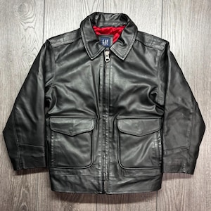 May include: Black leather jacket with a collared neckline, a full-length zip, and two front pockets. The jacket features a red lining and the GAP logo on the collar.