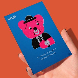 May include: A blue card featuring a pink bear character wearing a black suit, hat, and wristwatch. The card has the text "kapi" at the top left and "IT FIVE O'CLOCK SOMEWHERE" at the bottom. The card is held against an orange background.