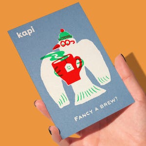 May include: A blue card with the word "kapi" in white. The card features a cartoon bird wearing a green hat and glasses, holding a red mug with a tea bag. The text "FANCY A BREW?" is below the illustration.