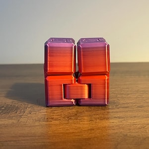 May include: A multi-coloured fidget toy in shades of red, orange, and purple. The cube-shaped toy is made of connected blocks that can be manipulated. The toy is designed to relieve stress and provide a tactile experience.