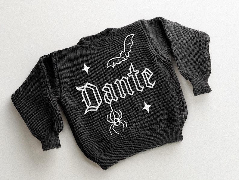 May include: Black knit sweater with the name "Dante" in white gothic lettering, a bat, spider, and stars. The sweater has long sleeves and a crew neck. The design is a Halloween or gothic theme.