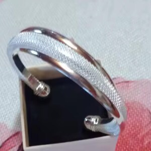 Peut inclure: Un bracelet jonc en argent avec une finition texturée. Le bracelet est ouvert et possède un fermoir à charnière.