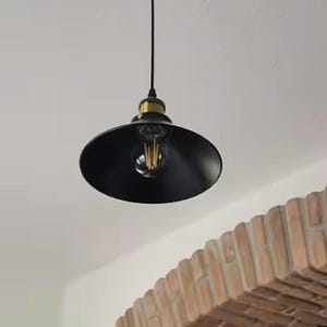 Puede incluir: Una lámpara colgante negra con acabado dorado y una bombilla transparente que cuelga de un techo blanco. La luz está colocada sobre un arco de ladrillo.