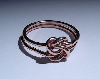 May include: A rose gold ring with a knot design. The ring is made of two bands that are intertwined.
