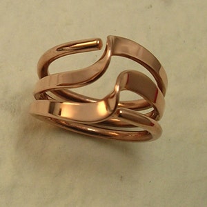 May include: A rose gold ring with three bands that are intertwined. The bands are smooth and shiny.