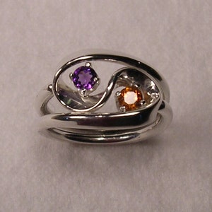 Può includere: Un anello d'argento con un design a spirale con una pietra preziosa viola e una pietra preziosa arancione.