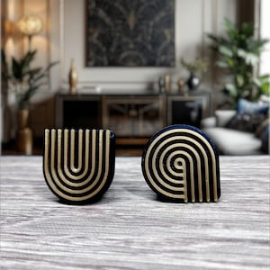 Può includere: Due tiretti per cassetti decorativi con un design geometrico. I tiretti sono in metallo nero con accenti dorati. I tiretti hanno la forma di una U e di una lacrima.