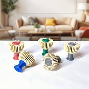 Könnte beinhalten: Eine Sammlung von fünf dekorativen Knöpfen mit einem einzigartigen Design. Jeder Knopf hat eine cremefarbene, fächerartige Oberseite und einen farbigen Sockel in Rot, Grün, Blau und Grau. Die Knöpfe sind auf einer weißen Oberfläche angeordnet.