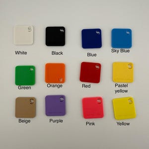 May include: A collection of square color swatches in various shades, including white, black, blue, sky blue, green, orange, red, pastel yellow, beige, purple, pink, and yellow. Each swatch has a small hole and text labels.