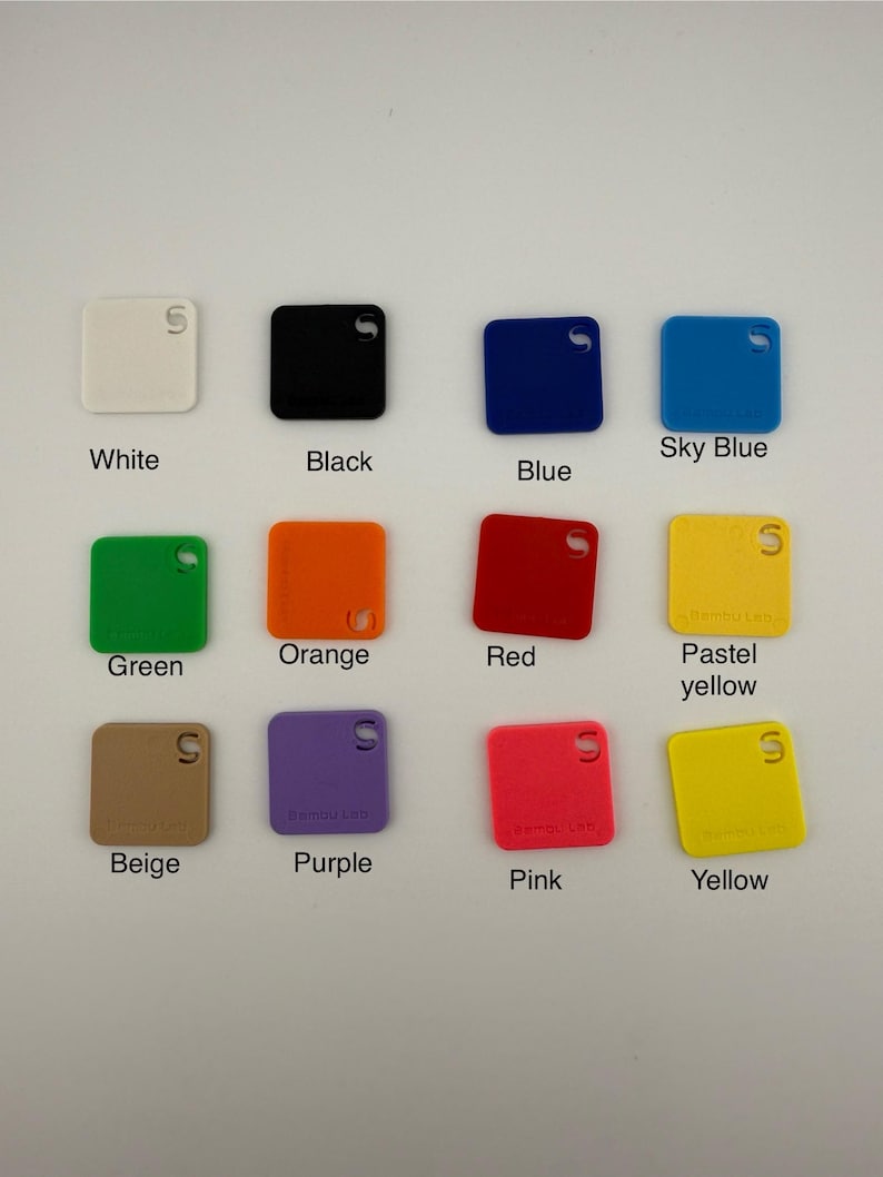 May include: A collection of square color swatches in various shades, including white, black, blue, sky blue, green, orange, red, pastel yellow, beige, purple, pink, and yellow. Each swatch has a small hole and text labels.