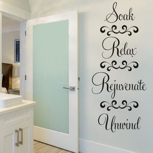 May include: White bathroom with double sinks and a white vanity. A frosted glass door leads to another room. A wall decal with the words "Soak, Relax, Rejuvenate, Unwind" is on the wall.