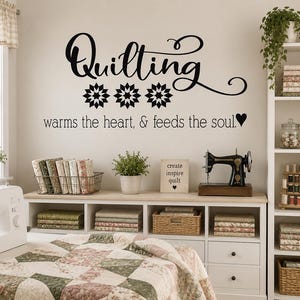 May include: A cozy quilting room with a white sewing machine, a vintage black sewing machine, and shelves filled with fabric. The wall features the text "Quilting warms the heart, & feeds the soul."