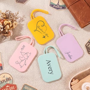 May include: Four colourful luggage tags in yellow, pink, lavender, and teal. Each tag has a loop for attachment and features personalised text. The yellow tag has a heart design and the names "Theodore & Alice". The pink tag has a map design and the initials "BSW".