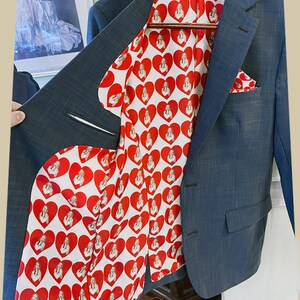 May include: A blue blazer with a red and white patterned lining featuring a repeated image of a woman. The lining is visible when the blazer is open.