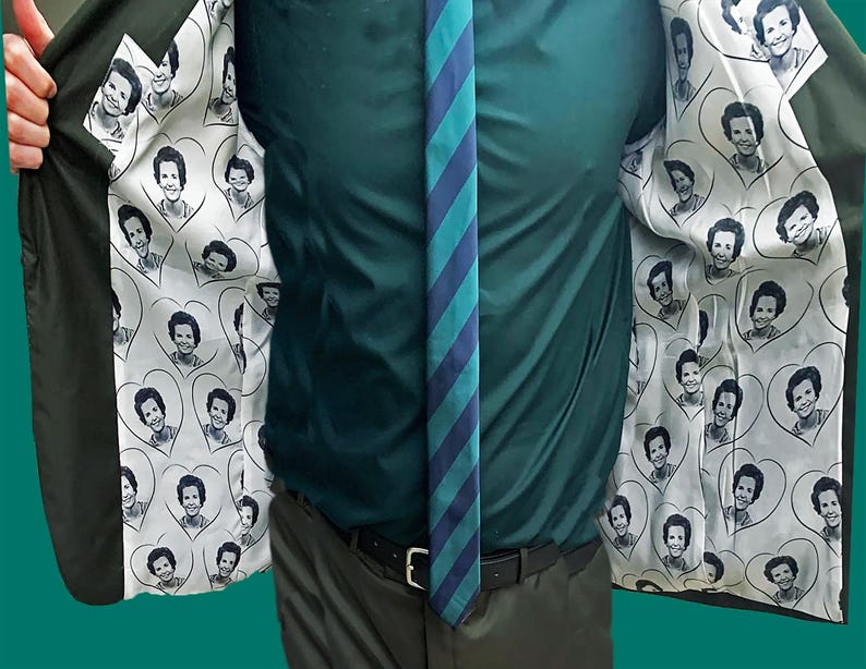May include: A dark green blazer with a white lining featuring a repeating pattern of a woman's face in a heart shape.