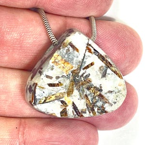 May include: A triangular pendant featuring a polished stone with a white base and embedded dark brown and golden-brown mineral inclusions. The stone is suspended from a silver-toned snake chain that attaches to the top corners of the pendant.