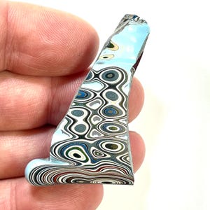 以下が含まれることがあります： 青、白、グレー、黒などの色が混ざった、ユニークな抽象的なアート作品。丸みを帯びたベースとギザギザのトップを持つ曲線的な形状をしています。デザインは同心円と波線が特徴です。