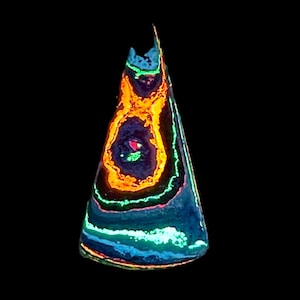 May include: A cone-shaped, glowing object with a dark background. The object features concentric rings of orange, green, blue, and red, creating a vibrant, layered effect. The top has a jagged edge, and the overall appearance is reminiscent of a gemstone.