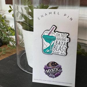 May include: An enamel pin featuring a turquoise and white drink with a straw, and the text "I'm not having a Baja Blast right now." The pin is on a white card with the words "ENAMEL PIN" at the top.