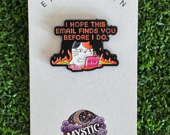 May include: An enamel pin on a white backing card featuring a calico cat at a laptop surrounded by flames. The text reads: I HOPE THIS EMAIL FINDS YOU BEFORE I DO. Below is a circular logo with a crescent moon, stars, and clouds labeled MYSTIC DESIGN CO.