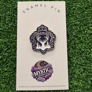 May include: An enamel pin on a white card. The pin features a deer with the text "YOU DO NOT YIELD" in a navy blue and white design. Below is a purple and white logo with the text "MYSTIC DESIGN CO." and a website address.