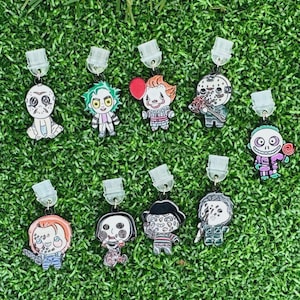 May include: A collection of eleven character-themed earrings, each with a unique design. The earrings feature various characters in a cartoon style, with a variety of colors and details. The earrings are displayed on a green, grassy surface.