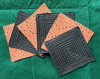 May include: A set of five square fabric coasters featuring alternating designs. Some coasters are solid black with orange spiral topstitching, while others are orange with black polka dots and black grid-like topstitching patterns.