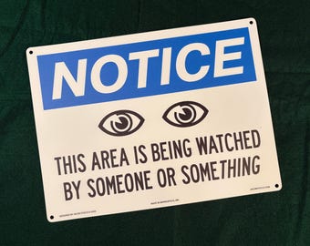 May include: A rectangular white metal sign with a blue header containing the word NOTICE in white text. Below are two black eye icons and the black text: THIS AREA IS BEING WATCHED BY SOMEONE OR SOMETHING. Small text at the bottom reads: DESIGNED BY JACOB STOLTZ 2020.