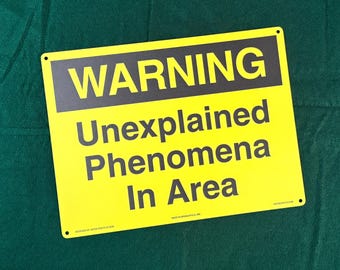 May include: A rectangular yellow metal sign with black text that reads WARNING Unexplained Phenomena In Area. The sign features a black horizontal bar at the top with the word WARNING in yellow capital letters and has four small corner holes.