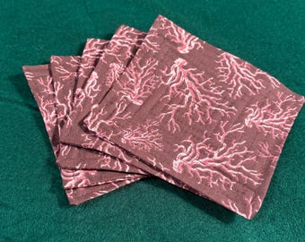 May include: A set of five square fabric coasters featuring a dark brown background with a repeating light pink coral branch pattern. Each coaster has visible straight-line machine stitching along the edges and across the surface.