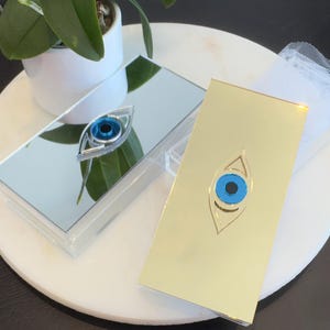 May include: A white ceramic mug with a black handle and the text "But First, Coffee" in a black, handwritten-style font. The mug is on a white surface.