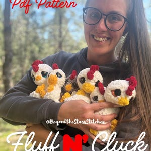 May include: A collection of crocheted chicken toys in white, yellow, and red, held in a person's arms. The toys have large eyes and red combs. The text "Pdf Pattern" and "Fluff N' Cluck" are visible in the image.
