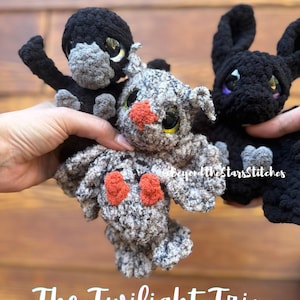 May include: A crochet pattern for three plush toys: a black bat, a gray owl, and a black dragon. The toys have large eyes and are held in a person's hands. The text "PDF Pattern" and "The Twilight Trio" are visible.