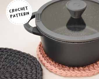 May include: Two crocheted pot holders, one in gray and one in pink, with a black pot and lid on top of the pink pot holder. The text "CROCHET PATTERN" is in a circle above the pot. The text "BY ORILYA" is at the bottom of the image. The text "+ Video Tutorial" is at the top of the image.