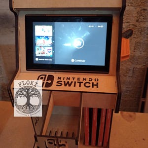 以下が含まれることがあります： ゲームカートリッジホルダーを内蔵した木製ニンテンドースイッチスタンド。スタンドは茶色に塗装されており、ニンテンドースイッチのロゴと「Nintendo Switch」の文字が書かれています。